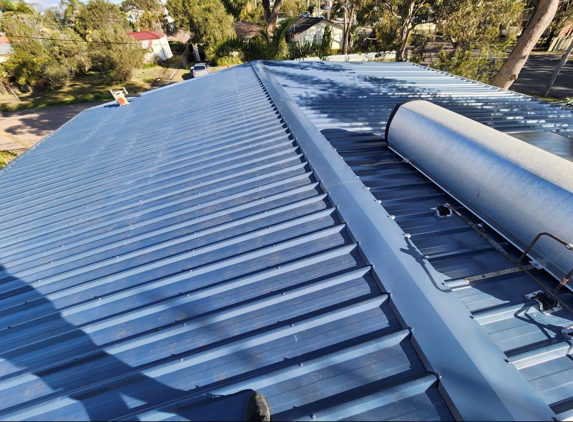 A newly installed blue-grey corrugated metal roof with ridge capping and a solar hot water tank