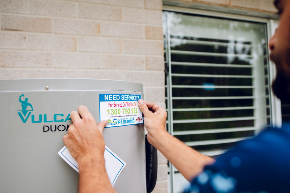 Creek to Coast Plumbing plumber fixing a service sticker to a Vulcan electric hot water system