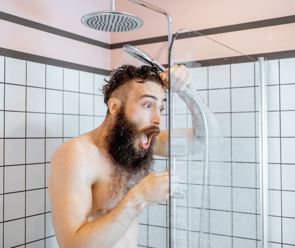 Man in the shower reacting as the water turns cold after the hot water runs out